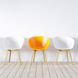 Imagen de tres sillas contra una pared blanca. La silla del medio es de color naranja.